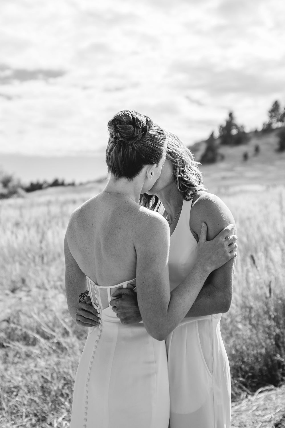 Black and white photo series showing two people in white dresses embracing in a sunny meadow.