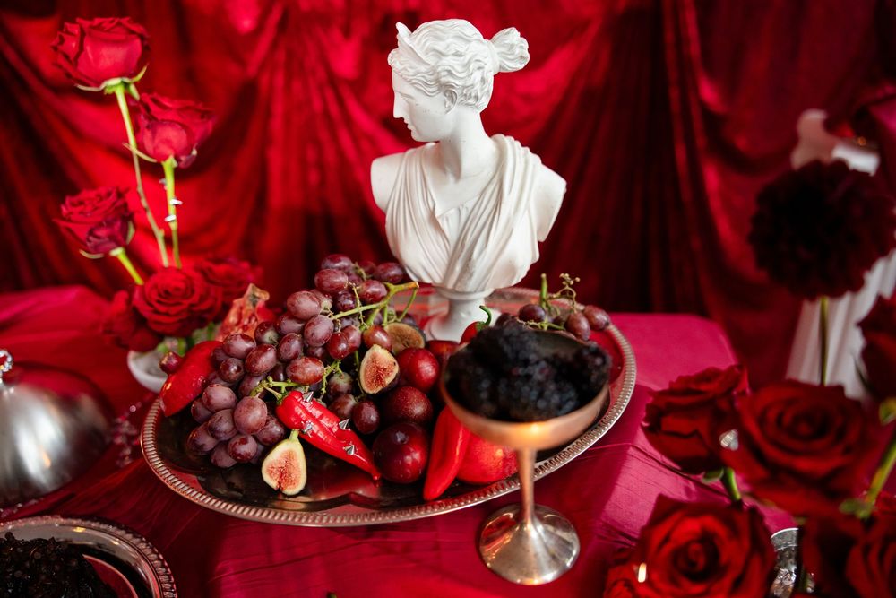 White classical bust sculpture on a platter with grapes and figs among red roses.