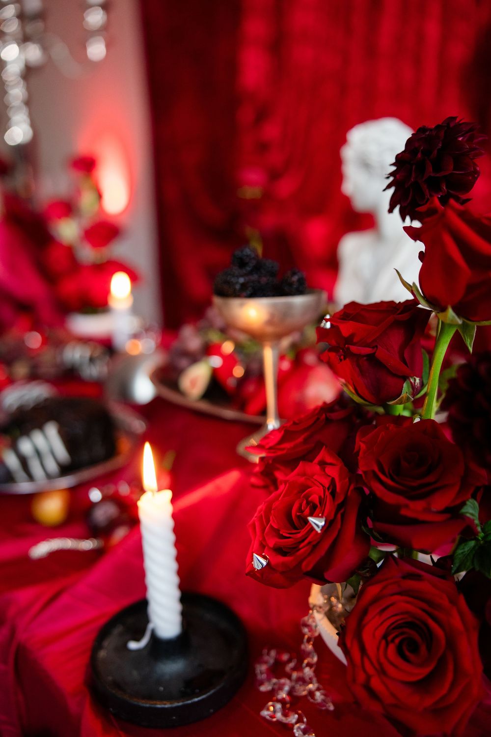 Red roses and white candle on a red tablecloth with decorative elements for a romantic gothic setting.