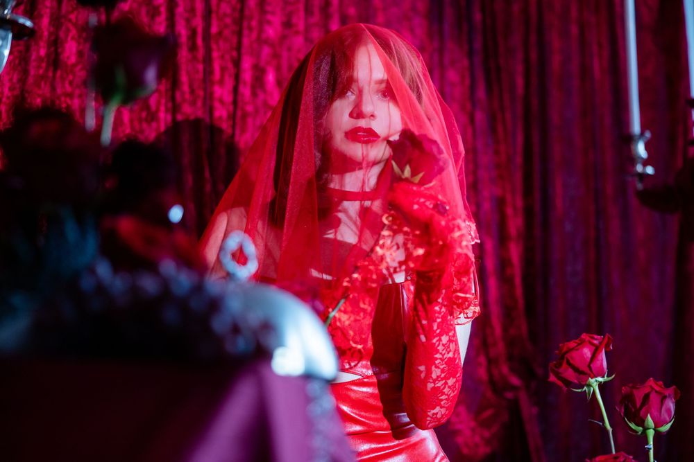Woman in red lace veil and gown posing dramatically in a dark red atmospheric setting.