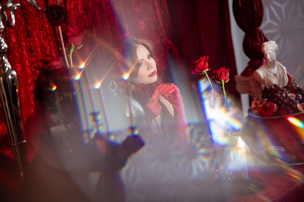 Woman in red dress reflected through crystal prism light effects at a decorated table.