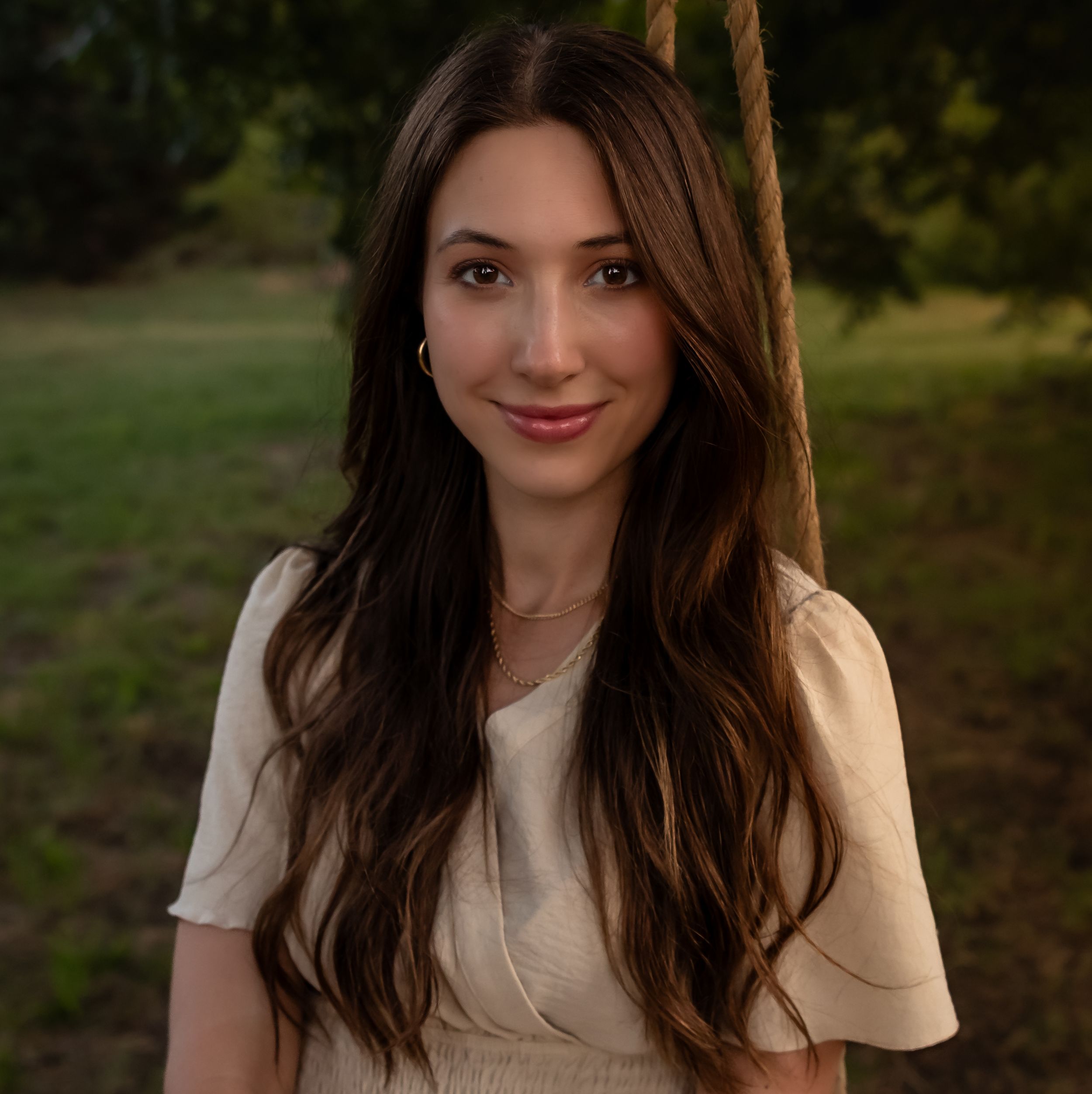 Portrait of woman in beige top against natural outdoor backdrop.