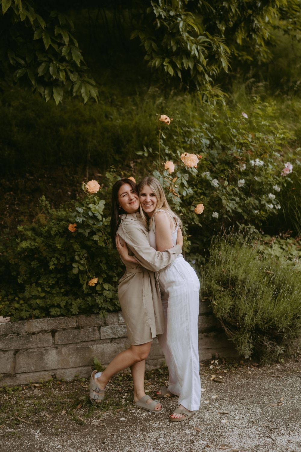 Friends sharing intimate moments and laughter against a backdrop of rose bushes.