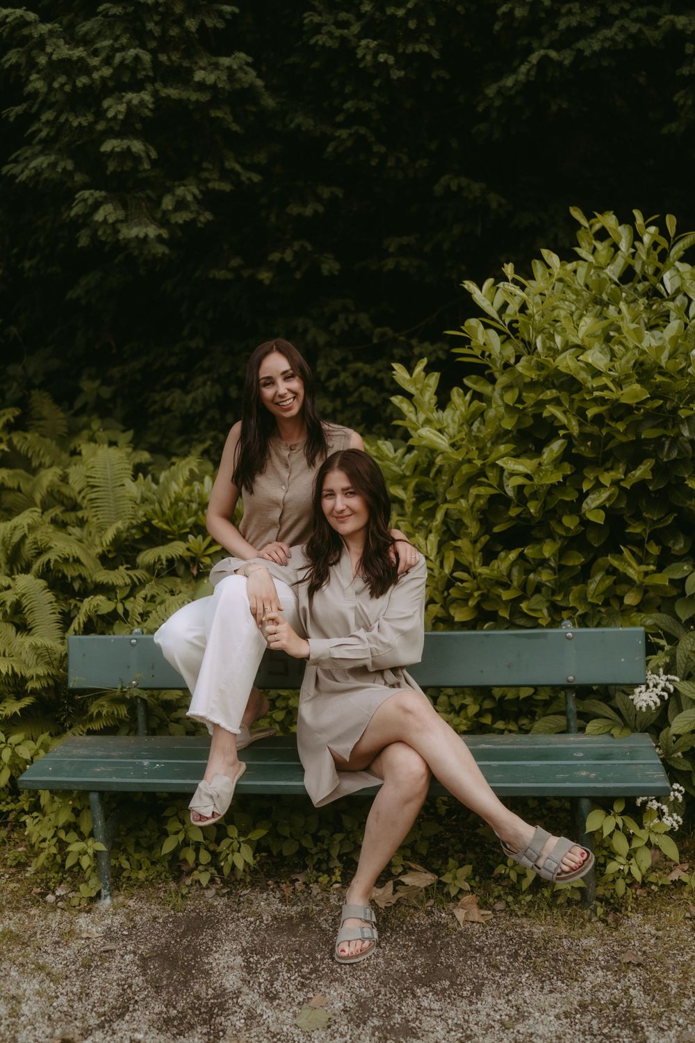 Playful friends lounging on a garden bench in neutral-colored outfits.