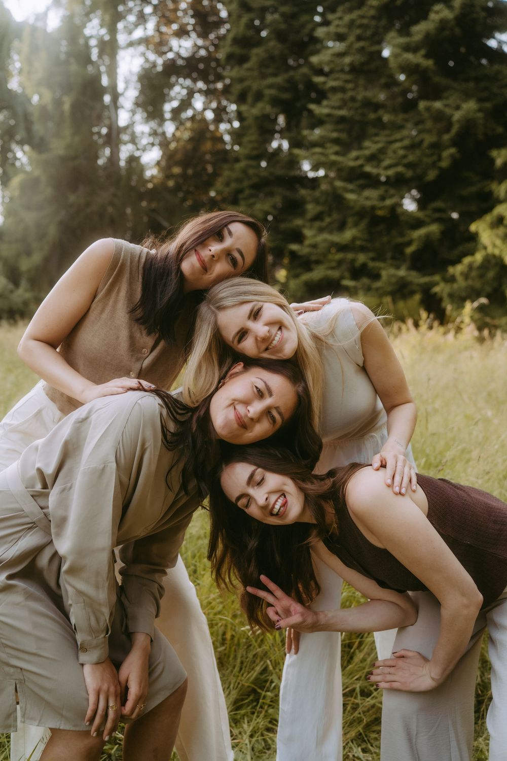 Group embracing and laughing together in casual neutral outfits against natural backdrop.