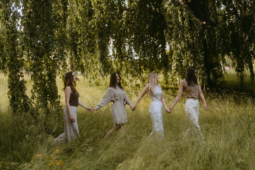 Friends walking through tall grass and trees in flowing neutral dresses.