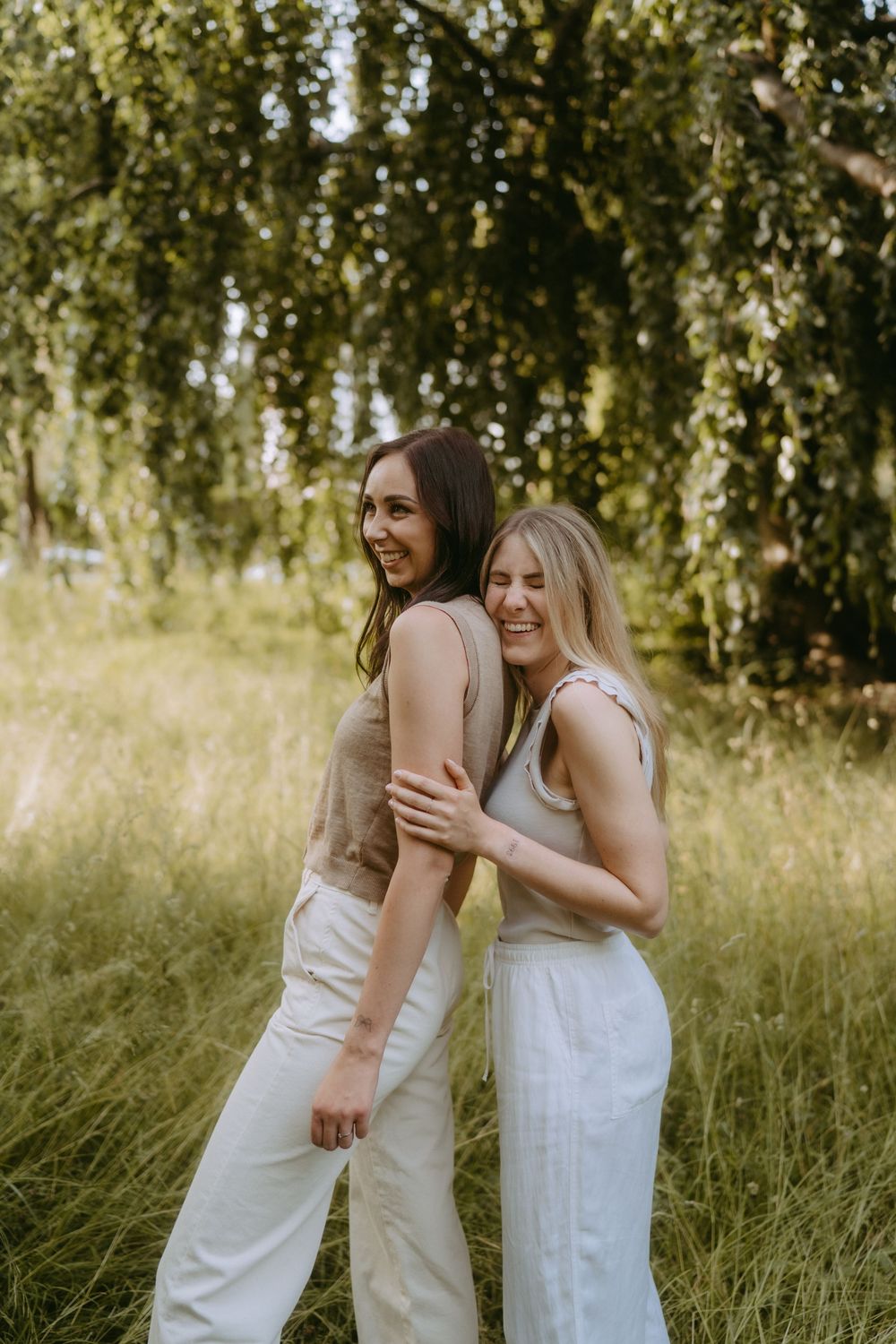 Friends sharing genuine laughter in coordinated white and beige outfits outdoors.