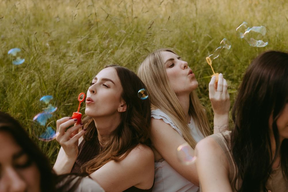 Friends blowing bubbles together in a golden sunlit garden setting.