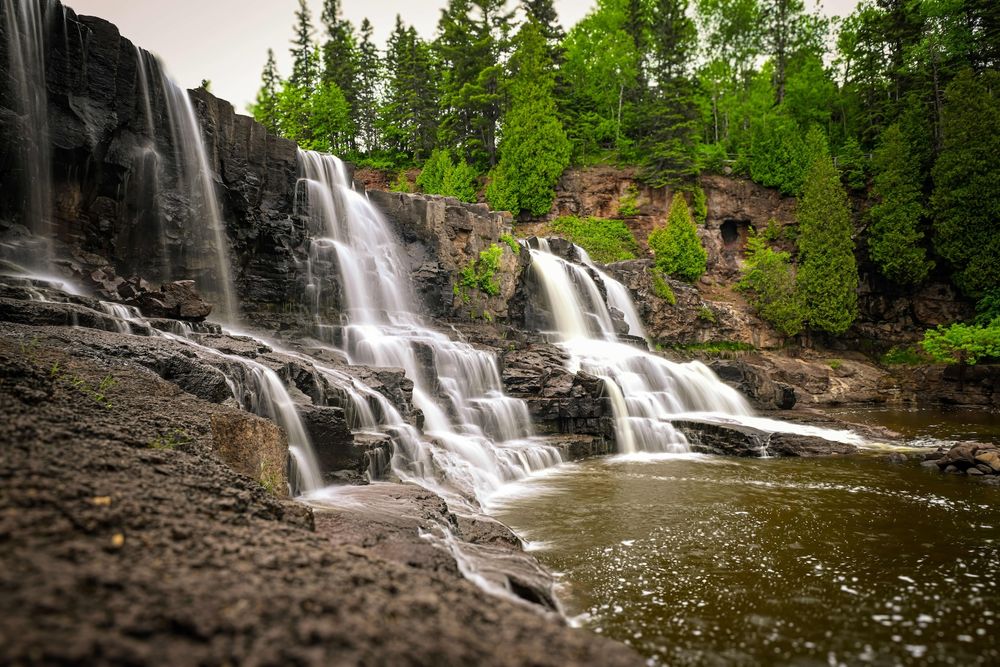 A series of seven panoramic shots showing a cascading waterfall flowing through a lush green forest landscape.