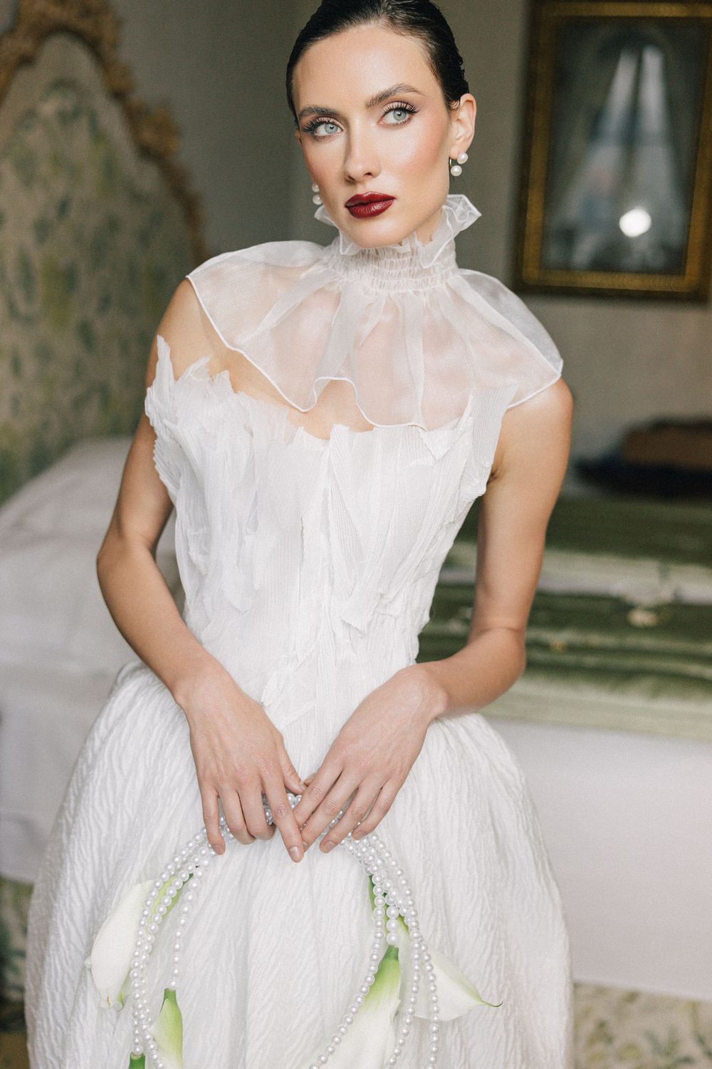 Elegant white bridal gown with ruffled neckline detail in vintage-style setting.