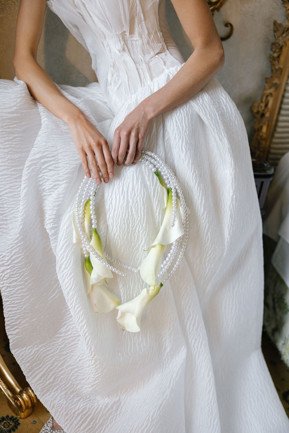 Close-up view of hands holding white calla lilies against a textured white wedding dress fabric.