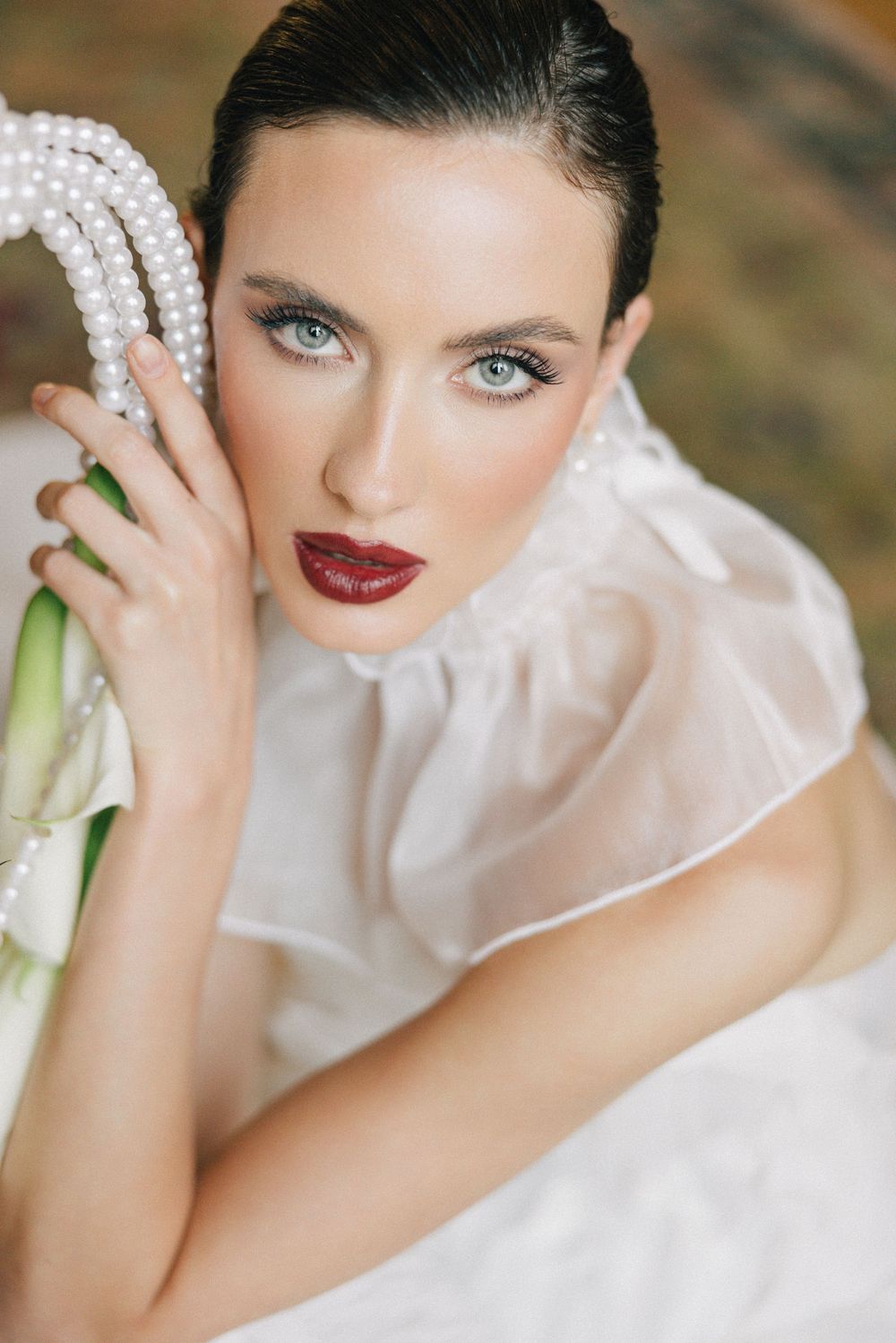 Close-up bridal portrait featuring dark lipstick, pearl accessories and high-neck white gown.