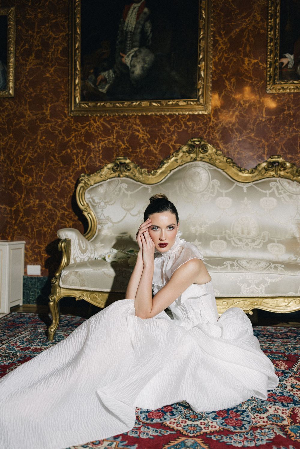 Elegant bridal portrait on an ornate sofa with floral carpet and gilded baroque wall decor.