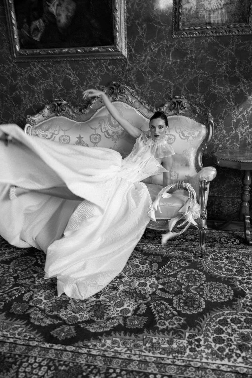 Artistic black and white photo of flowing white dress in motion against patterned carpet.