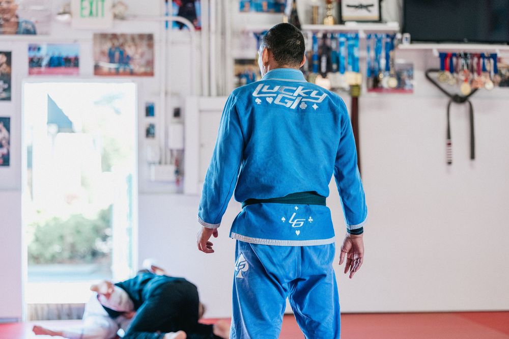 Martial arts students in blue uniforms practice techniques on a training mat in a bright studio space.