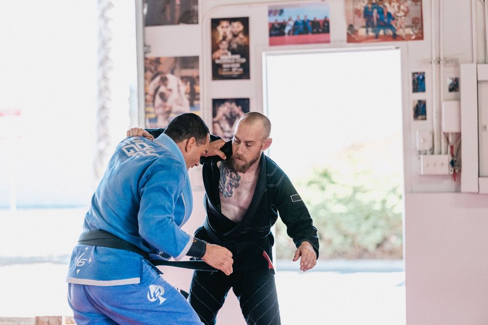Two martial artists practicing grappling techniques on blue mats during a training session.