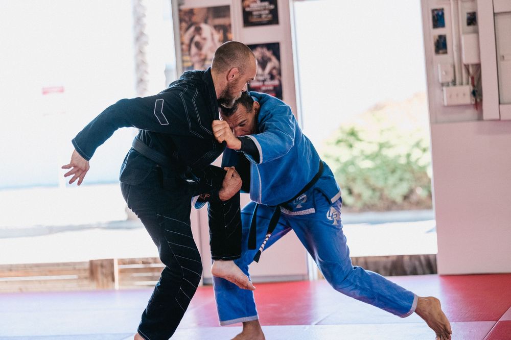 Two martial artists practicing judo throws and grappling techniques on red training mats.