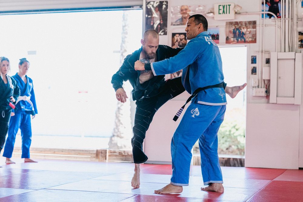 Students practice martial arts techniques on blue mats in a bright training studio.
