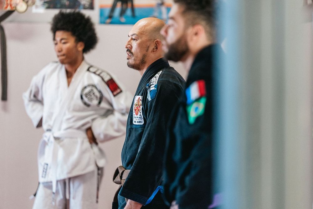 Students practice martial arts techniques together in a training studio wearing traditional white and black uniforms.
