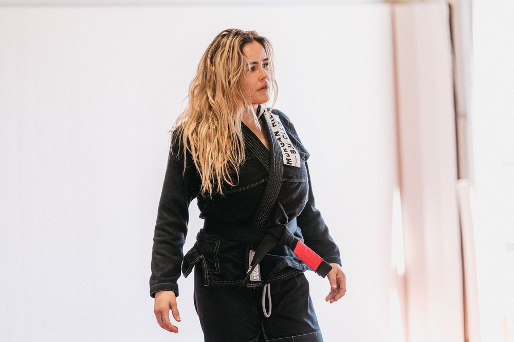 Woman in black martial arts uniform demonstrates self-defense moves in a training studio.