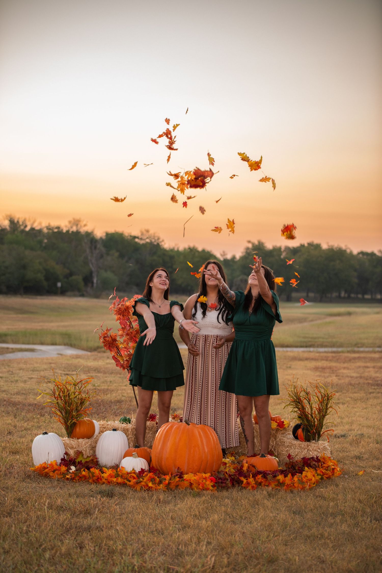 People enjoying a fall photoshoot tossing autumn leaves in the air while surrounded by pumpkins at golden hour.
