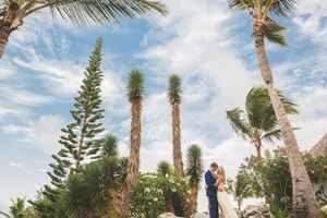 A romantic beach wedding ceremony under swaying palm trees with a bright blue sky and ocean backdrop.