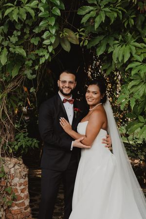 A happy couple shares joyful moments during their wedding photoshoot in front of a lush green garden wall.