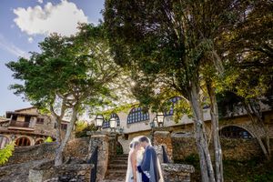 A rustic outdoor wedding venue with tall trees and stone architecture creates a romantic garden atmosphere.