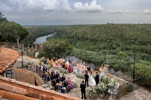 Tourists gather at a scenic viewpoint overlooking a lush river valley with dense green vegetation and cloudy skies.