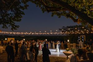 String lights illuminate an outdoor wedding reception setup with tables and chairs under a starry night sky.