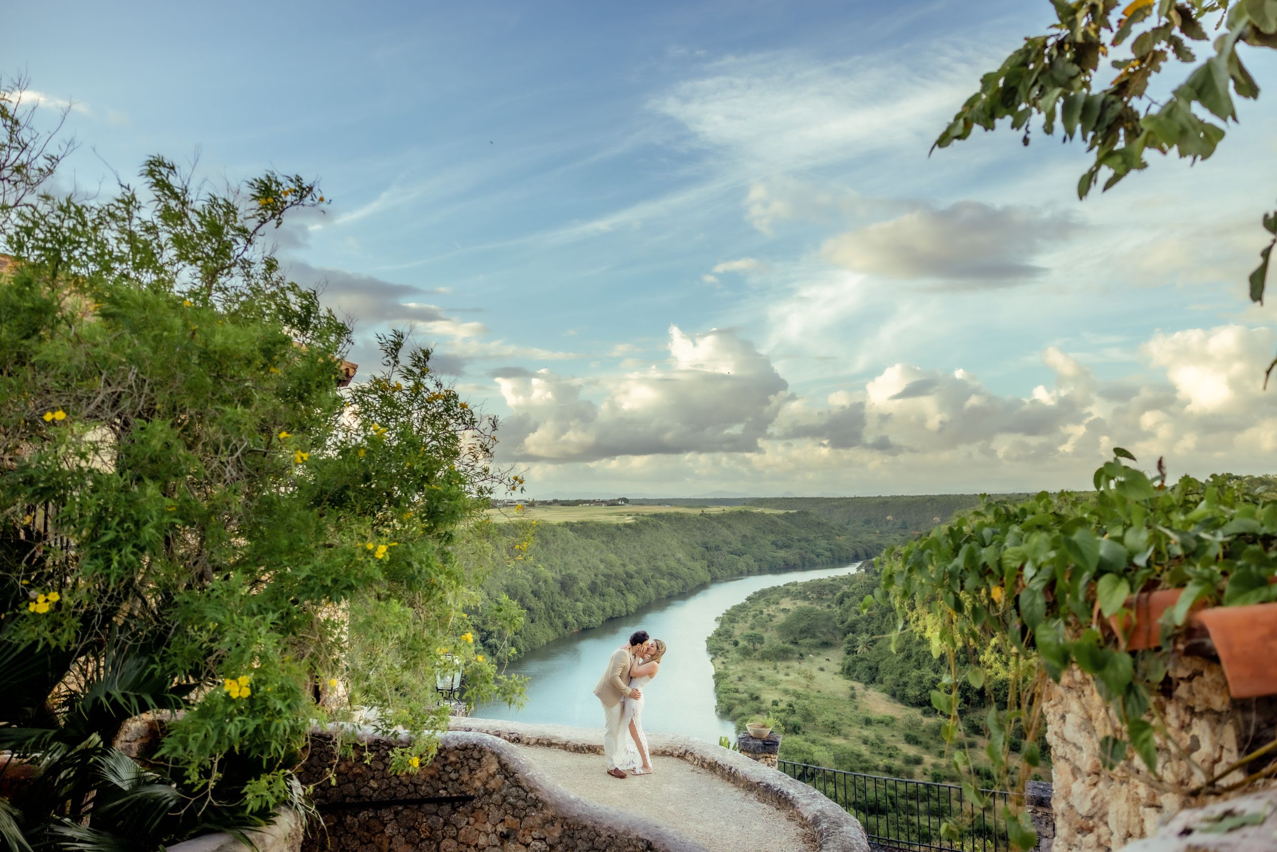 Scenic panoramic view of a winding river valley with lush green forests and cloudy blue skies.