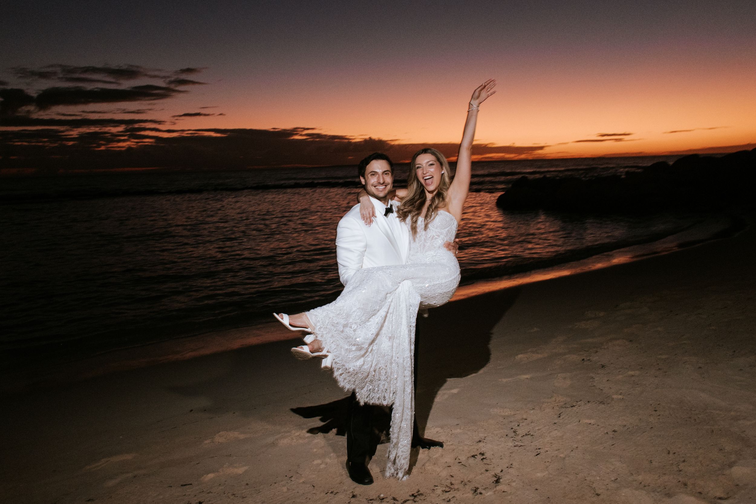 Silhouetted couple dances on beach during dramatic orange and purple sunset over ocean waters. Minitas Beach