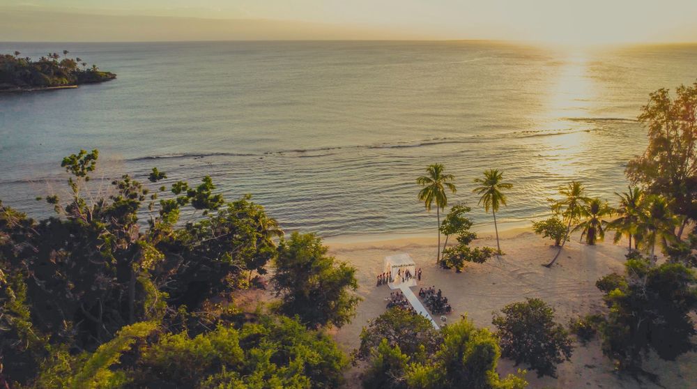 Aerial view of a pristine tropical beach with palm trees and golden sunset lighting over calm waters.