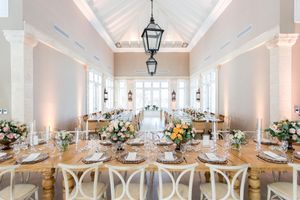Elegant white wedding reception venue with crystal chandeliers, lantern sconces, and table settings in a bright airy space.