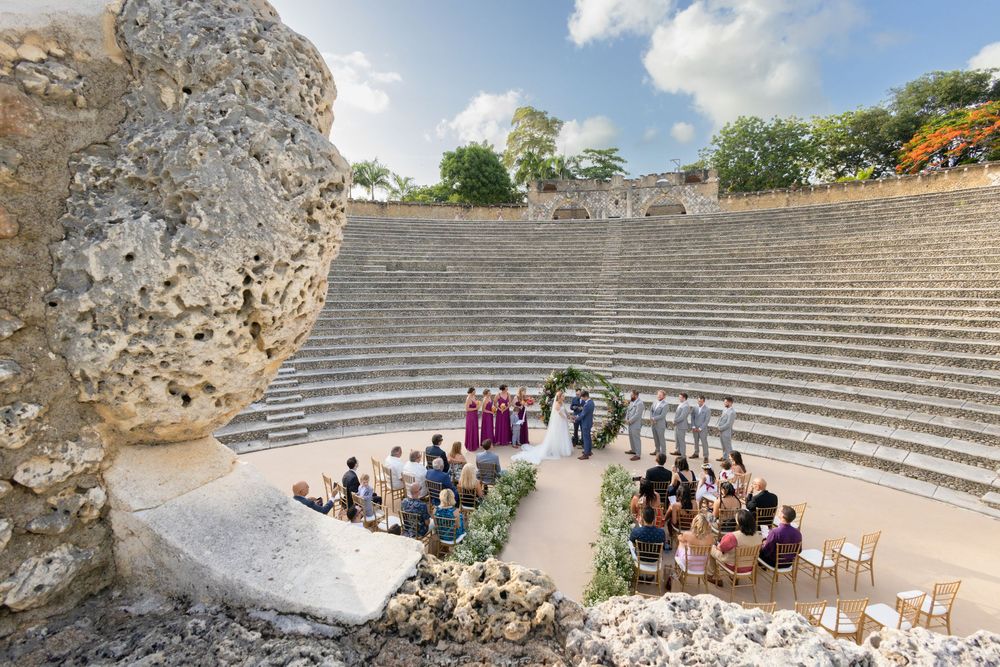 Ancient stone amphitheater steps and ruins under blue sky with scattered clouds and visitors exploring the historic site.