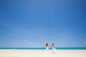 Two people walk along a pristine white sand beach with turquoise water and clear blue sky in the Caribbean.