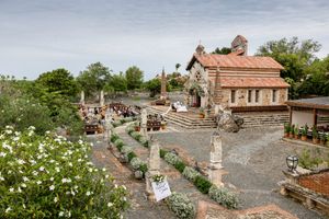 A panoramic view of an ancient stone village with terracotta roofs and blooming flowers in the Mediterranean landscape.