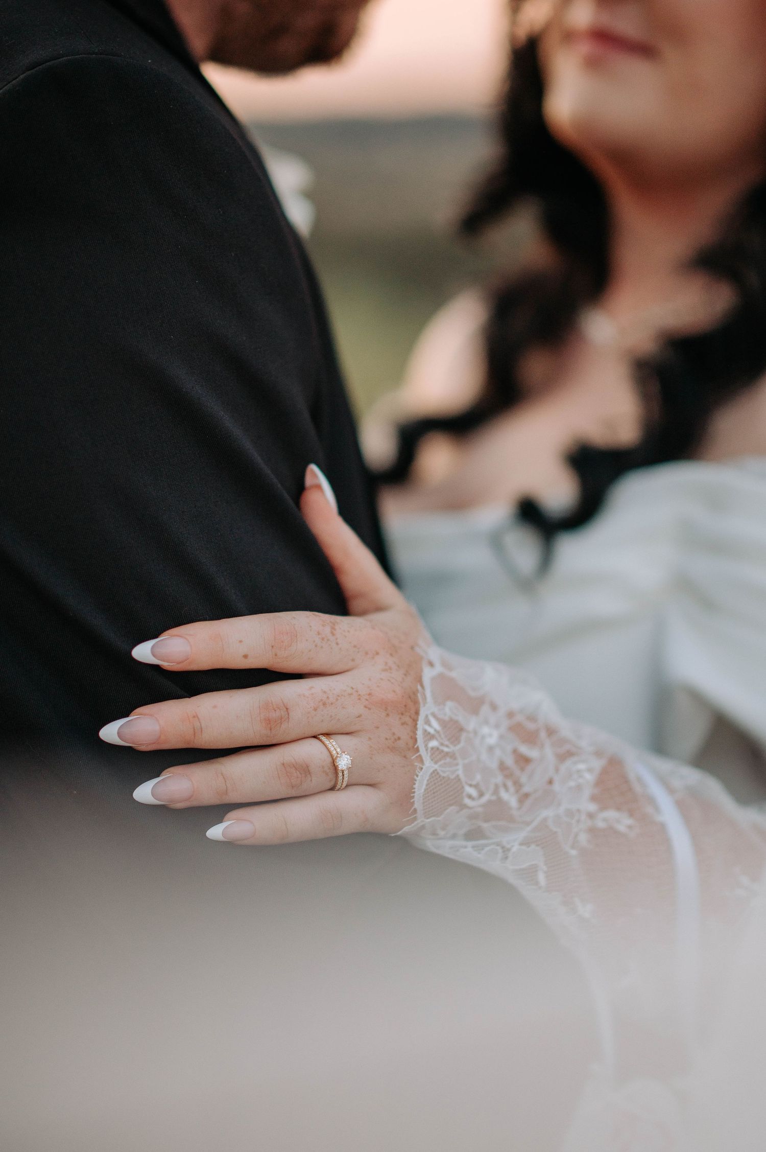 A delicate white lace bridal glove adorned with intricate floral patterns is displayed against a soft blurred background.