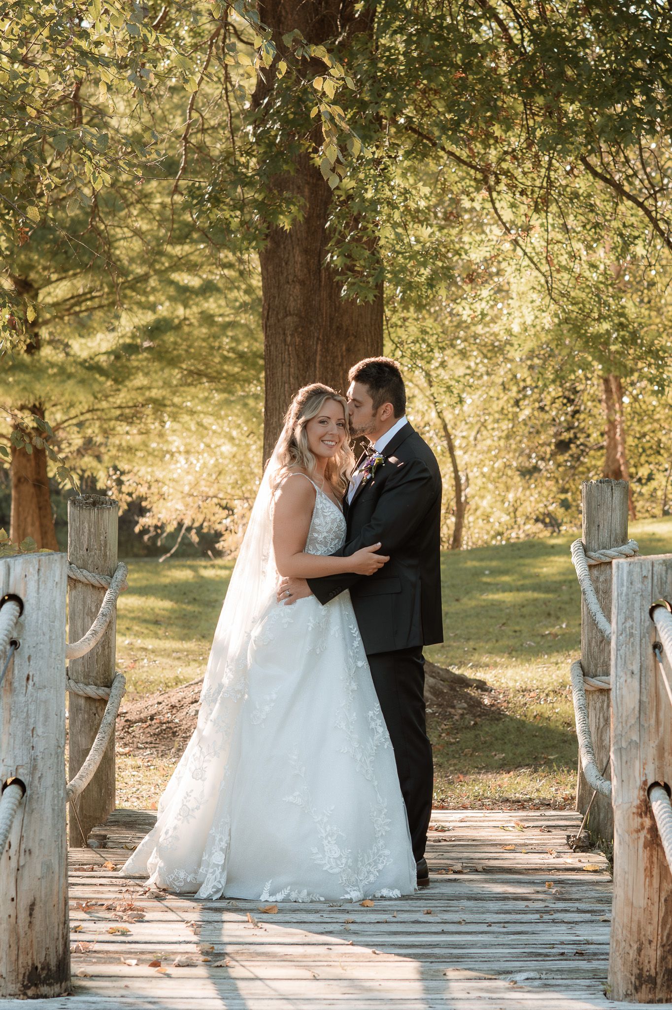 A romantic wedding couple shares an intimate moment on a rustic wooden bridge surrounded by autumn trees.