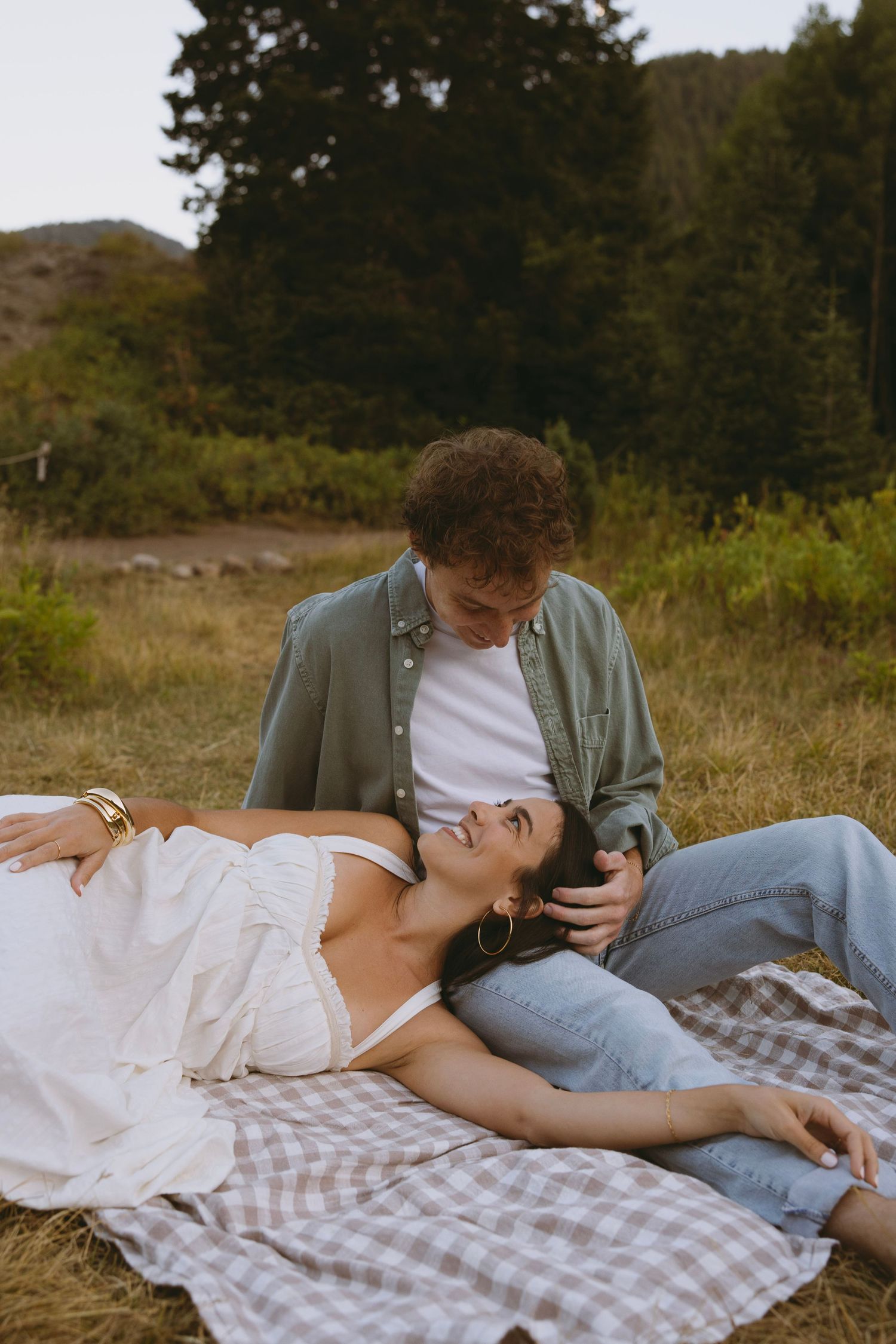 A couple shares an intimate moment along a forest path lined with evergreen trees and birch during a wedding photo session.