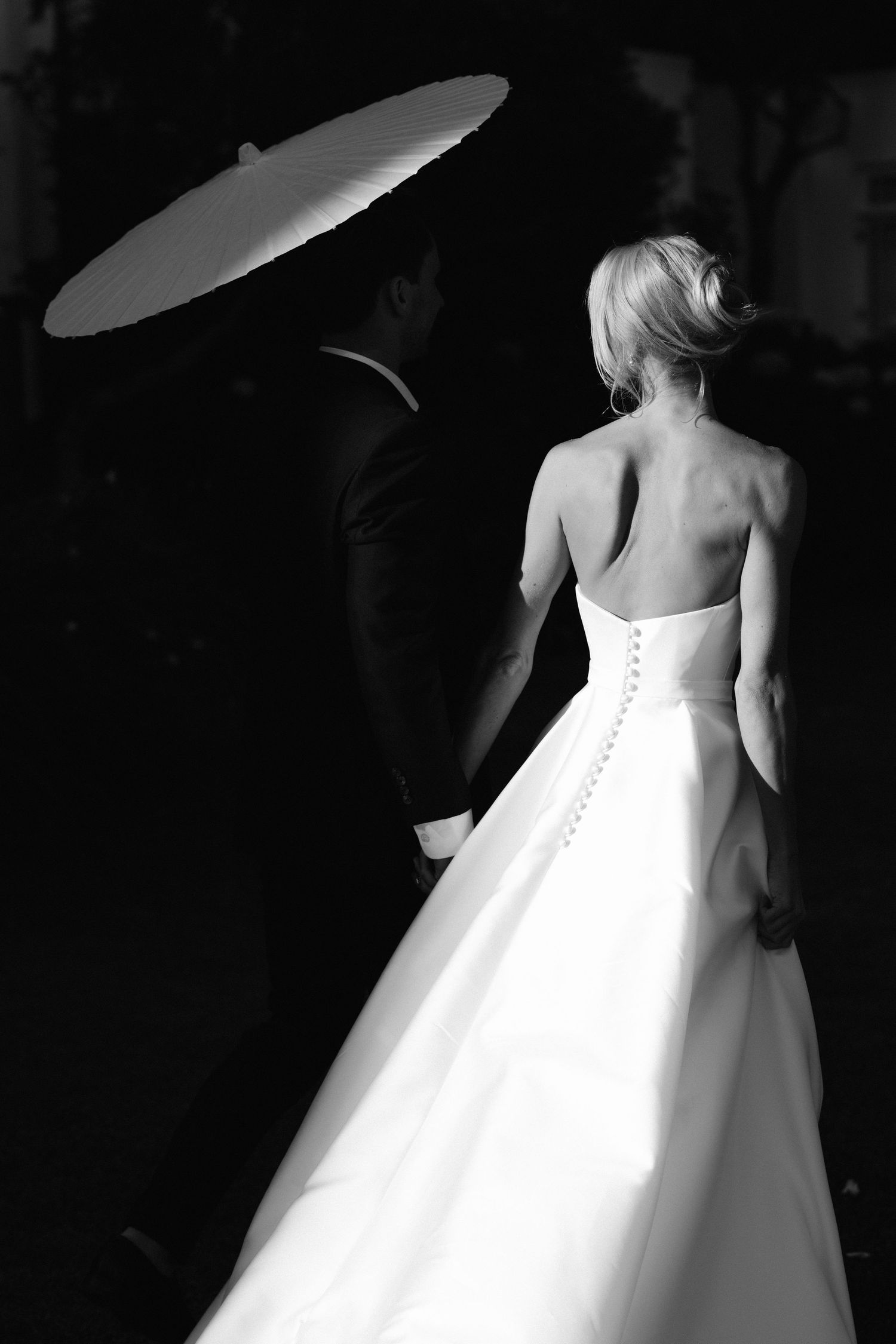 Back view of an elegant white wedding dress with button details photographed in dramatic black and white lighting.