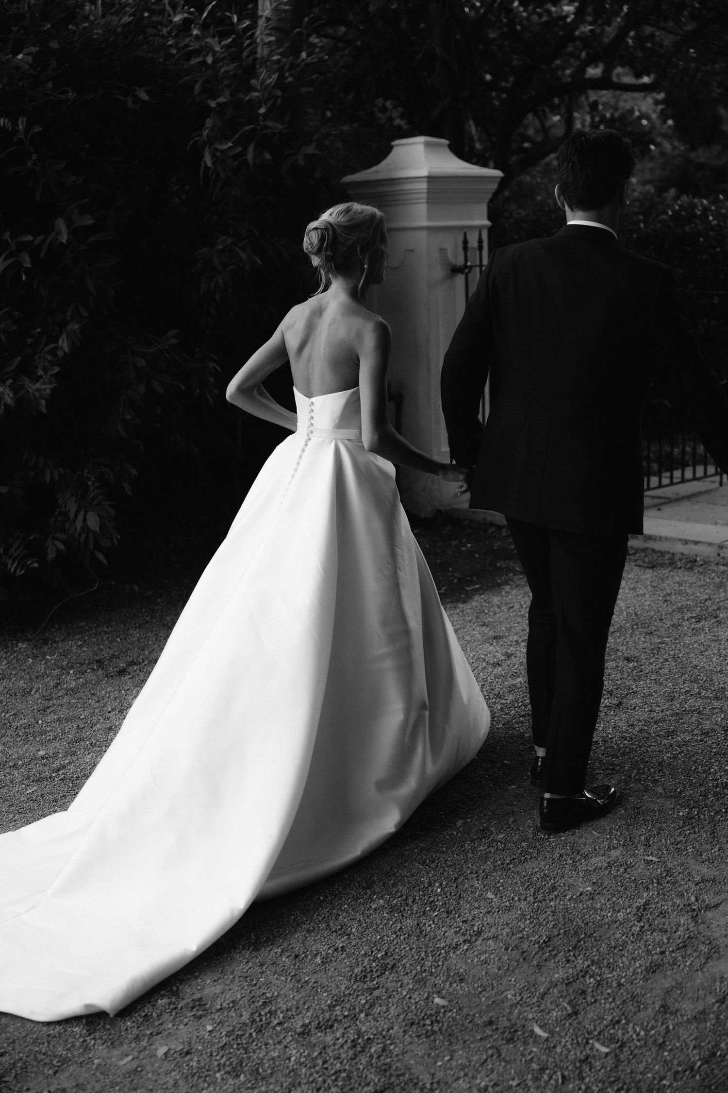 Black and white wedding photos showing the dramatic silhouette of a bride's flowing gown as the couple walks together.