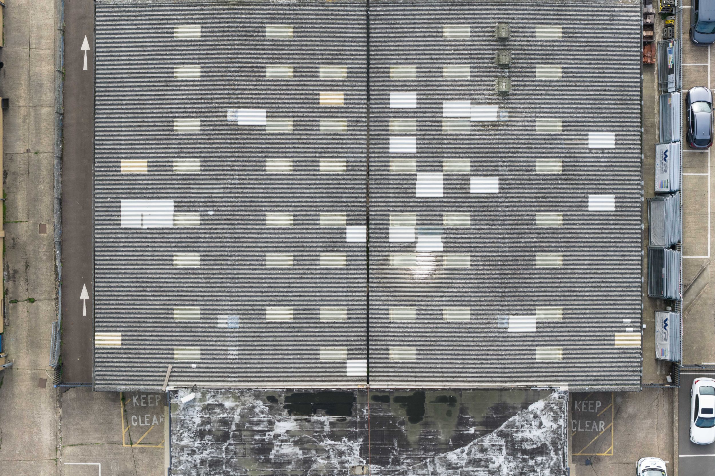 Aerial view of a large industrial warehouse rooftop with white rectangular skylights arranged in a grid pattern.