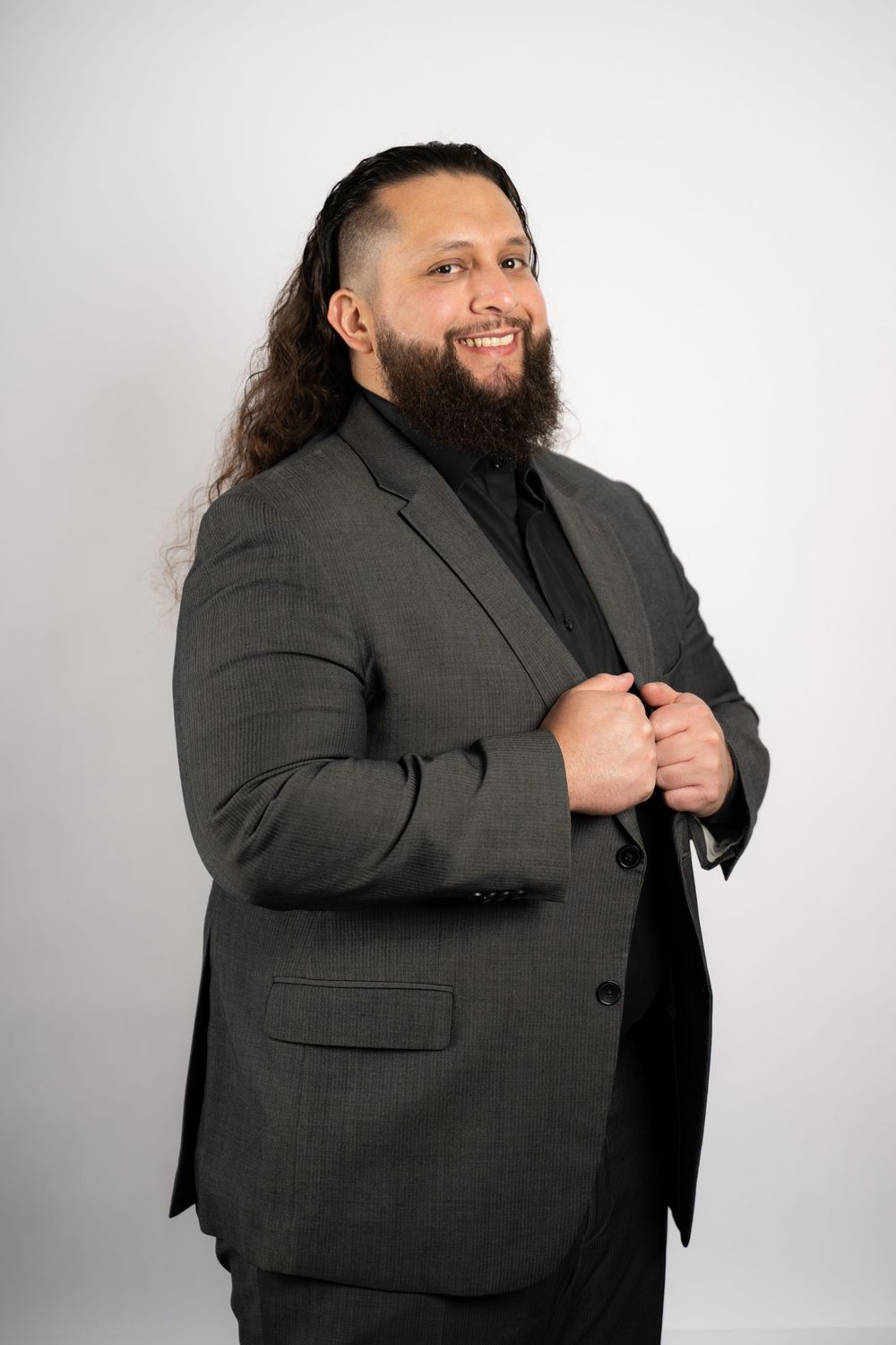 A person in a dark suit jacket poses confidently against a white studio background.