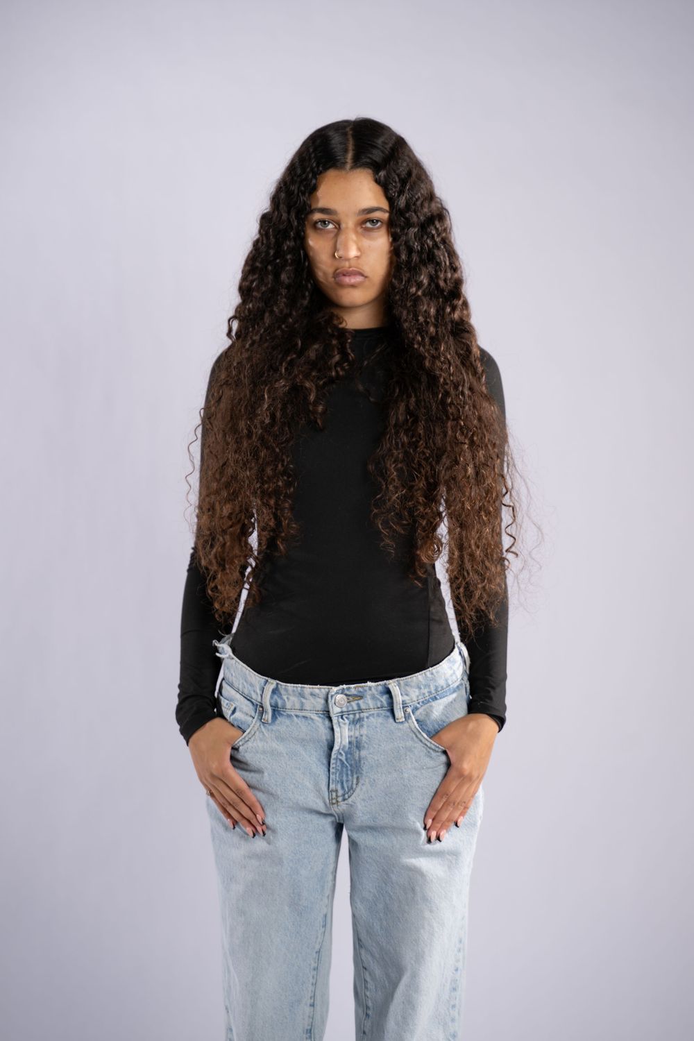 Fashion portrait against white background featuring black top and light wash denim.
