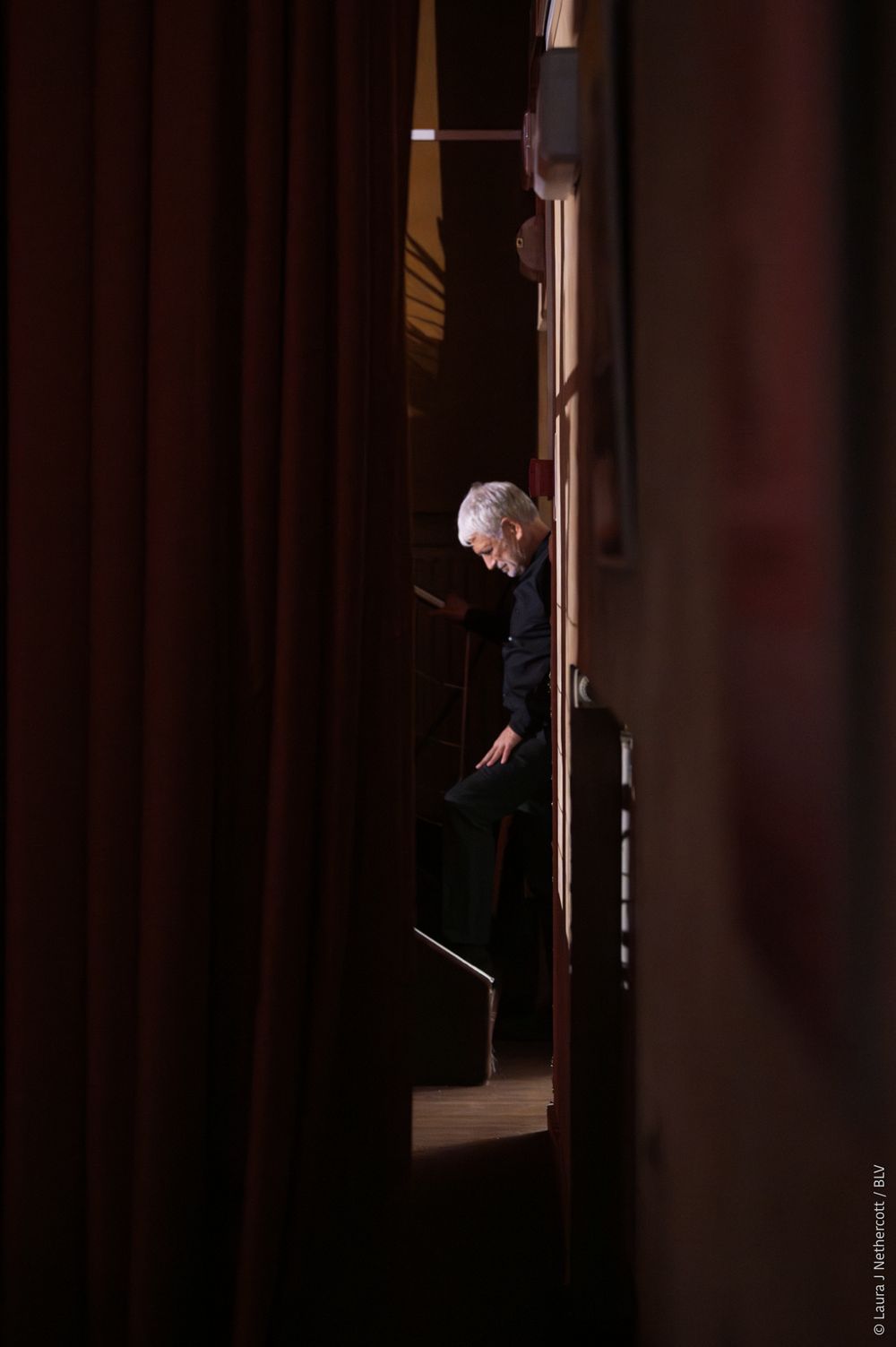 A person peers through a dimly lit doorway in a dark interior space.