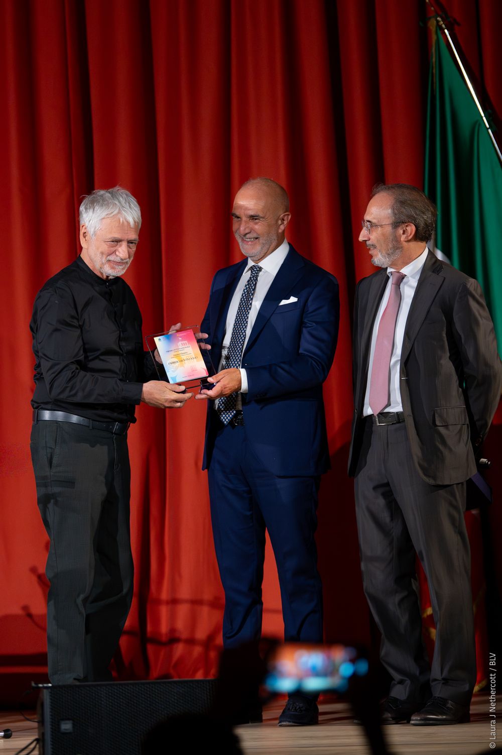 A series of formal award presentation moments on stage with red curtain backdrop showing various handshakes and exchanges.