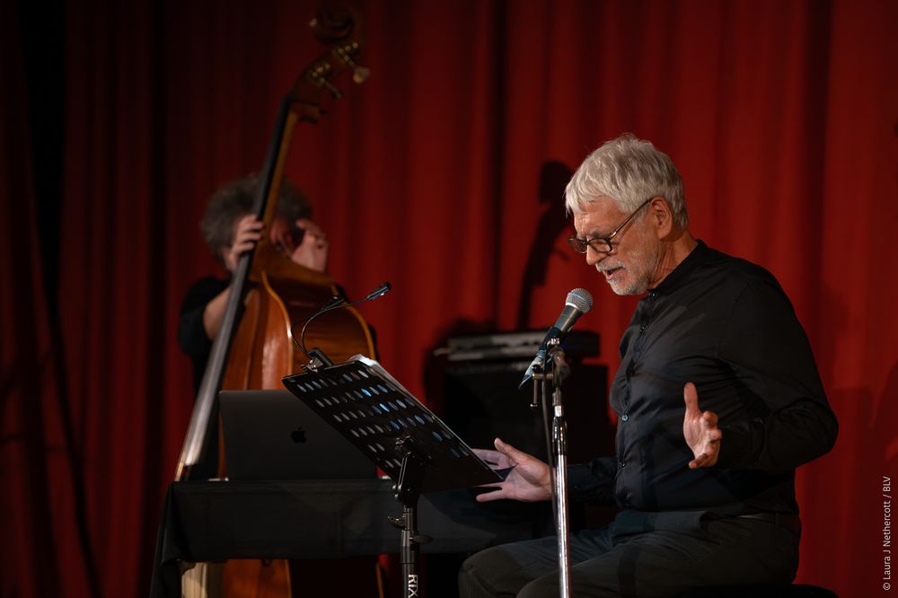 Musician playing double bass against red curtain backdrop in performance setting.