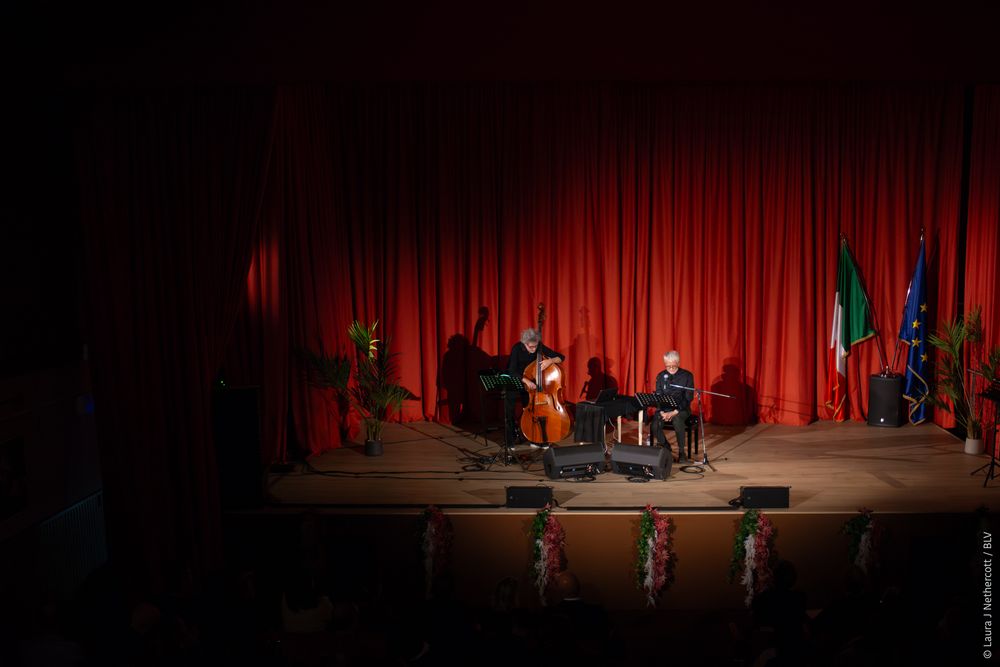 Musicians perform on a dimly lit stage with red curtains during a jazz concert.