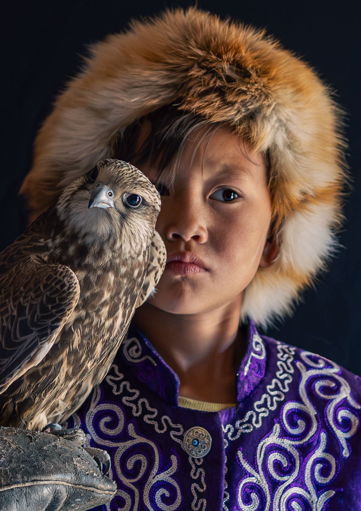 A person in a purple embroidered coat with fur trim poses with an owl in a dramatic portrait series.